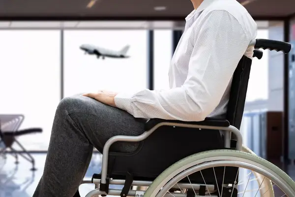 Person seated in a wheelchair near an airport area with a plane in the background