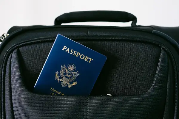 A passport partially visible in the pocket of a black carry-on bag