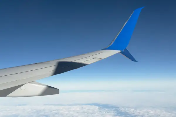Airplane wing with a blue fin flying above the clouds under a clear sky