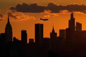 A plane flies over the New York City skyline at sunset 