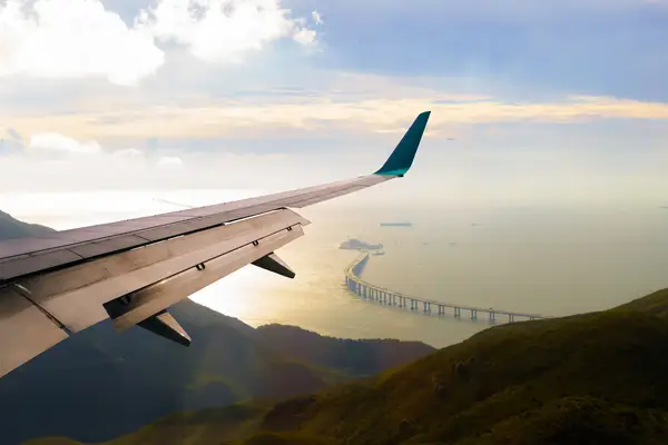 Aircraft wing over mountains, bridge visible extending across water