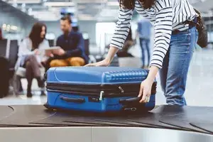 A person retrieves a suitcase from an airport baggage carousel, with others seated in the background