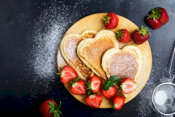 valentines day breakfast table with heart shaped pancakes and strawberries, top view