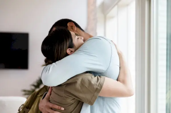sad mid adult female soldier hugs her husband goodbye as she leaves for military duty