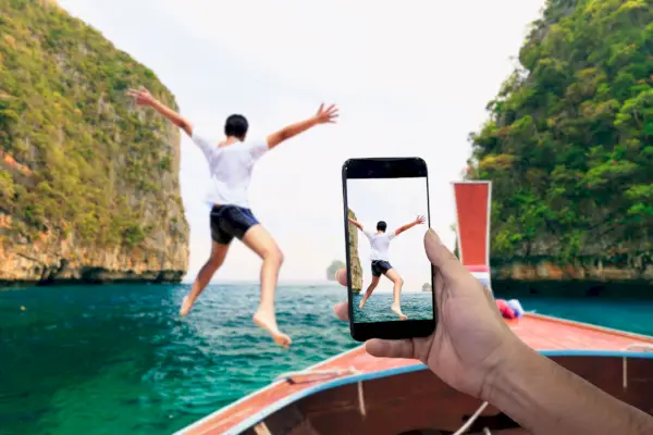 Smartphone photographing Asian young man jumping from boat into the Andaman Sea, Thailand