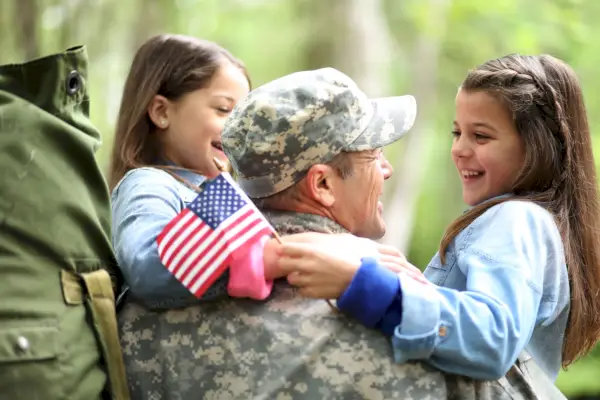 family welcomes home a usa army soldier the children excitedly hug father holding american flags