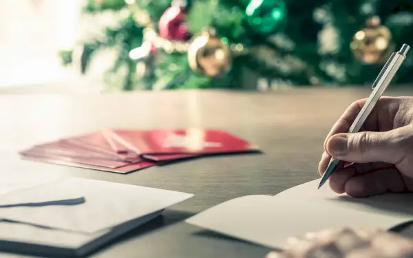 writing christmas card messages in front of a holiday tree