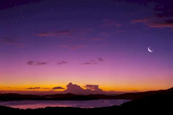 crescent moon visible at twilight in a purple and orange sky over body of water