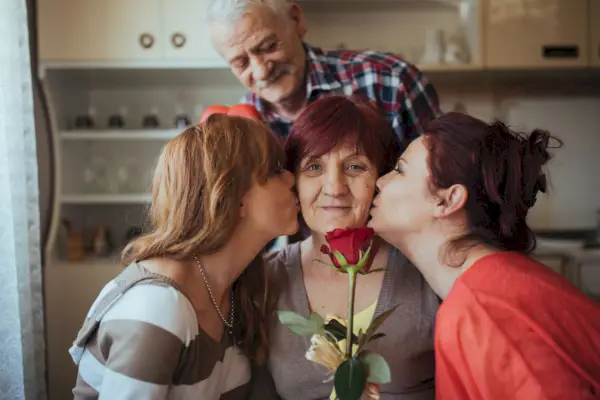 two grownup daughters kissing their mom