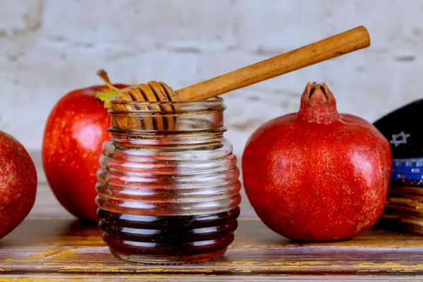 pouring honey on apple and pomegranate with honey symbols of jewish new year rosh hashanah
