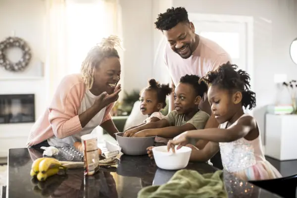 young family mixing cookie dough together at home in the kitchen