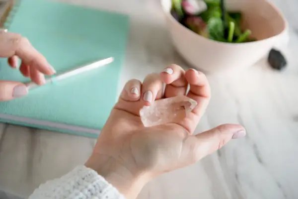 hand of woman holding healing crystals with notebook in background