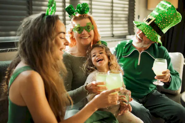 happy smiling family ready for st patricks day party people wearing green clothes, green hats, deely bobber, and glasses with clover shaped family drinking green non alkohol soda water and celebrating saint patricks day