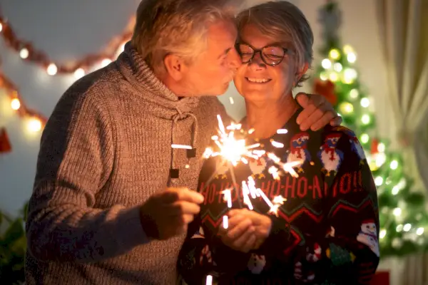 an affectionate kiss between elderly wife and husband who celebrate christmas with sparks lights and christmas tree in the background