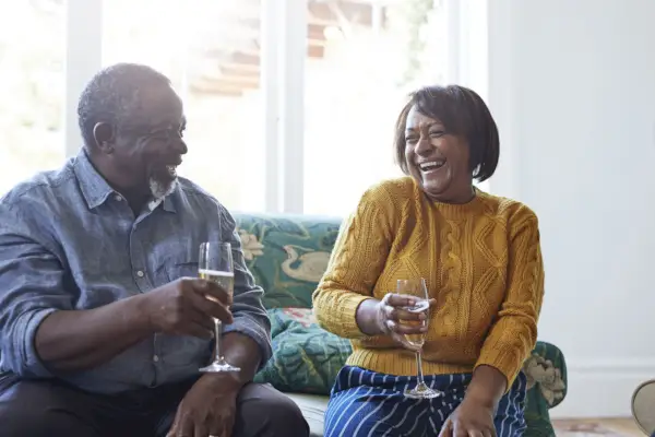 cheerful male and female friends enjoying champagne while talking at home during christmas celebration