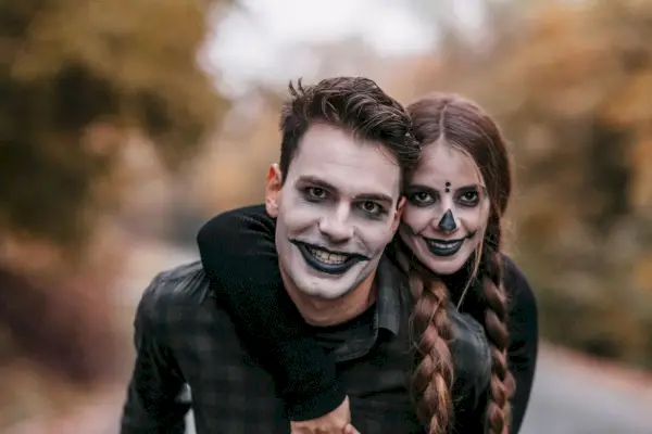 smiling man in halloween makeup carrying smiling woman in halloween makeup on a piggyback