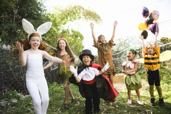 excited children in a back yard in halloween costumes as a bunny, magician, bee, flower and more