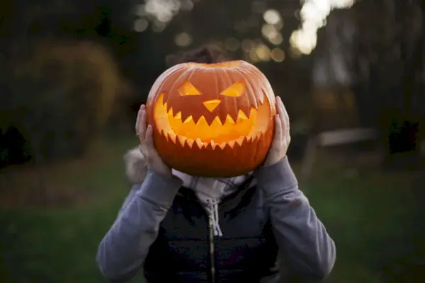 a girl holding carved and illuminated halloween pumpkin in front of her head