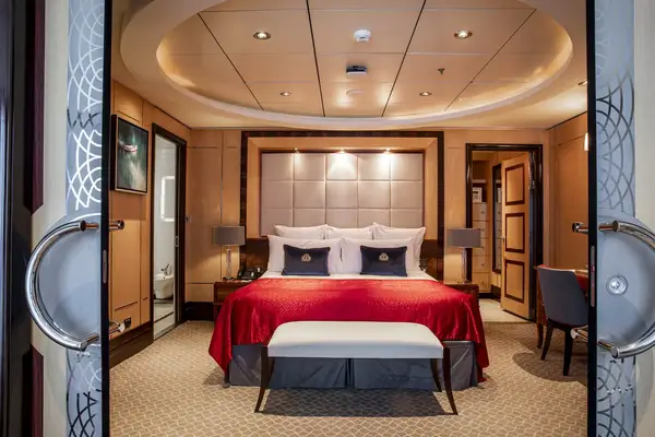 A luxurious bedroom with a queensized bed decorative pillows seating nearby and sophisticated lighting and paneling