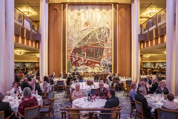 A dining area with people seated at round tables in front of an artistic mural