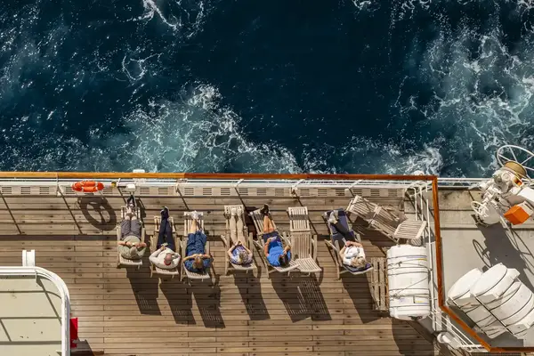 A group of people relaxing on lounge chairs on a ships deck next to a view of the ocean
