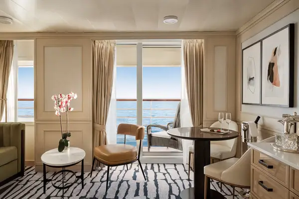 Luxury suite interior with seating, a table, and a view of the ocean through glass doors