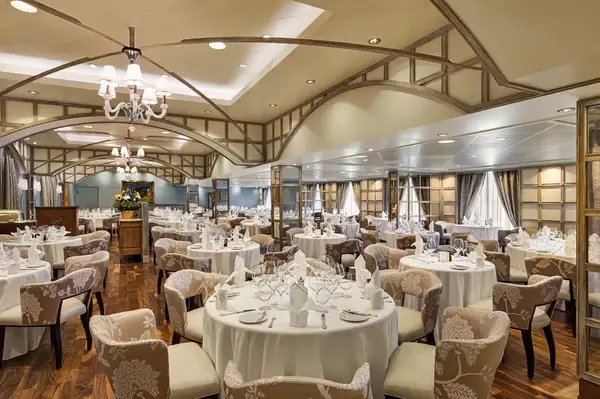 Elegant dining room setup with round tables and white chairs arranged in a spacious room with wooden flooring and ceiling arches