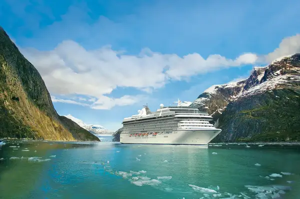 A cruise ship sailing through a scenic fjord with mountains on either side and ice in the water