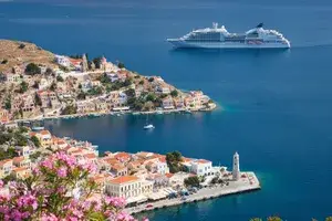 A cruise ship near a seaside town with historic buildings and a clear blue harbor flowers in the foreground