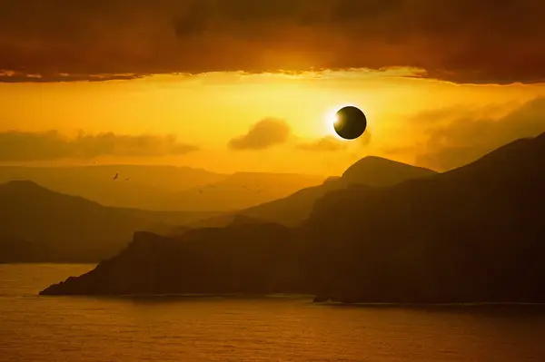 A solar eclipse over a coastal landscape with sea and mountains