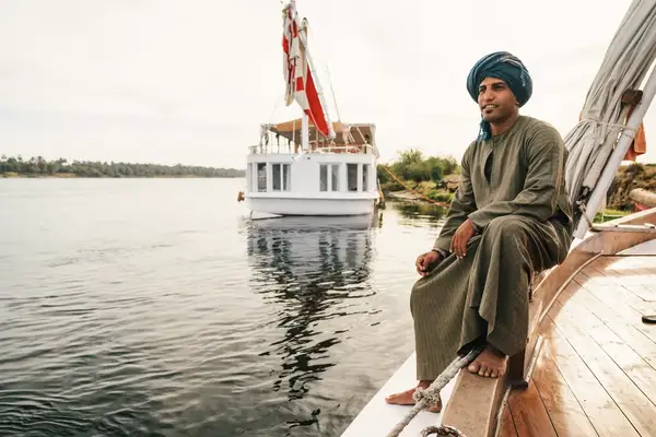 A boat crew member on the side of a traditional sail boat on the Nile