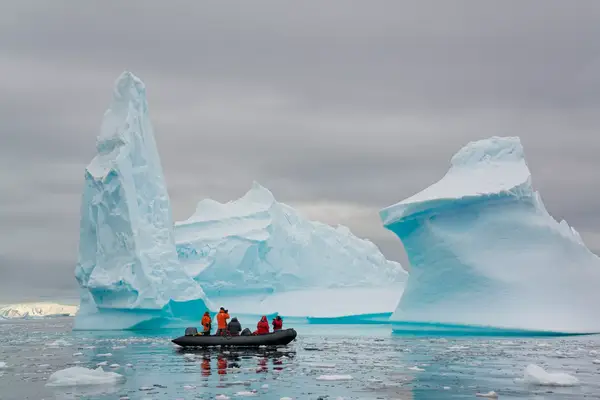 People in small inflatable Zodiac rib boats passing towering sculpted icebergs on the calm water around small islands of the Antarctic Peninsula