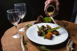 A hand pours sauce onto a dish of caribou and peas