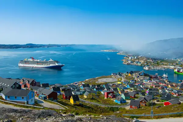 A cruise ship docked near a colorful town by water in Greenland