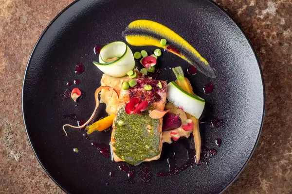 A dish of salmon and vegetables plated on a black dish