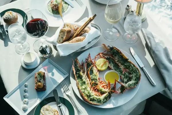 A table set with gourmet food and drink including lobster halves bread and wine on white tablecloth