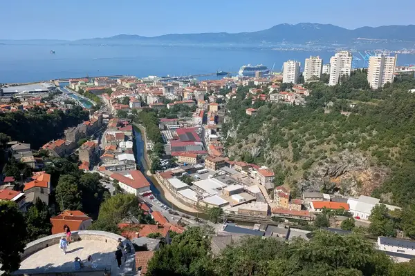 Scenic view of Rijeka Croatia featuring urban buildings surrounding forested hills and the Adriatic Sea in the background