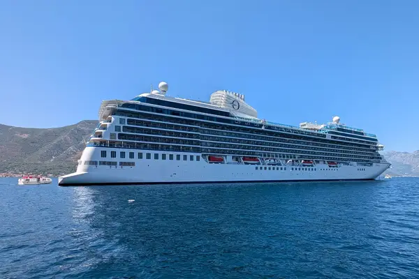 A large cruise ship floating on calm water with mountains in the background