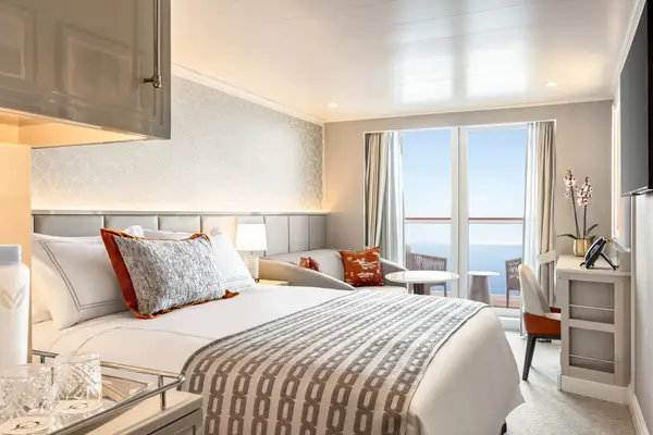 Luxury cruise ship stateroom with a balcony view of the sea featuring a bed seating area desk and decor