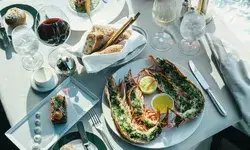 A table set with gourmet food and drink including lobster halves bread and wine on white tablecloth