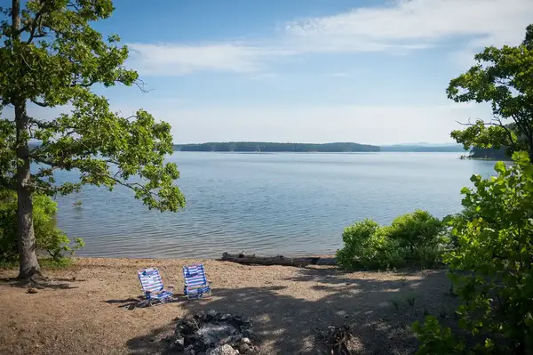 Two empty chairs overlooking a lake surrounded by trees