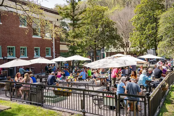 Outdoor seating area with people dining patio umbrellas and a brick building in the background