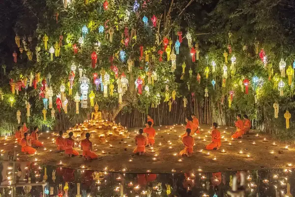 Brightly colored lanterns hanging in a tree above monks in orange robes