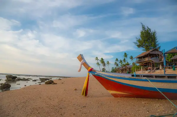 A traditional boat on a sandy beach with palm trees and buildings in the background
