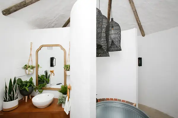 A rustic bathroom with a round tub wooden counter plants and unique light fixtures