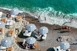 Blue and white striped beach umbrellas and people on a beach in Italy