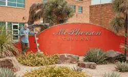 A person stands near the McPherson Cellars sign, landscape surrounding it with plants and rocks