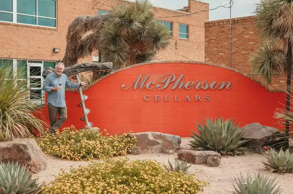 A person stands near the McPherson Cellars sign, landscape surrounding it with plants and rocks