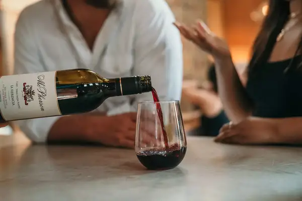 Wine being poured into a glass, two people talking in the background