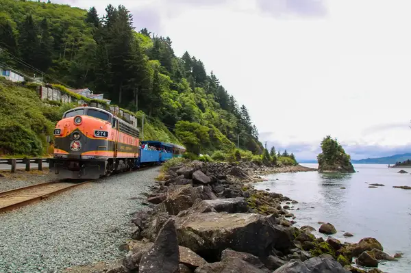 A scenic train traveling beside a rocky coastline and forested hills
